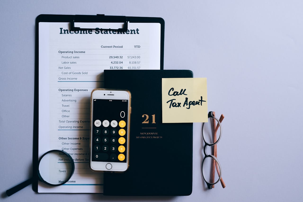 Top view of a desk with income statement, phone calculator, and tax reminder note.